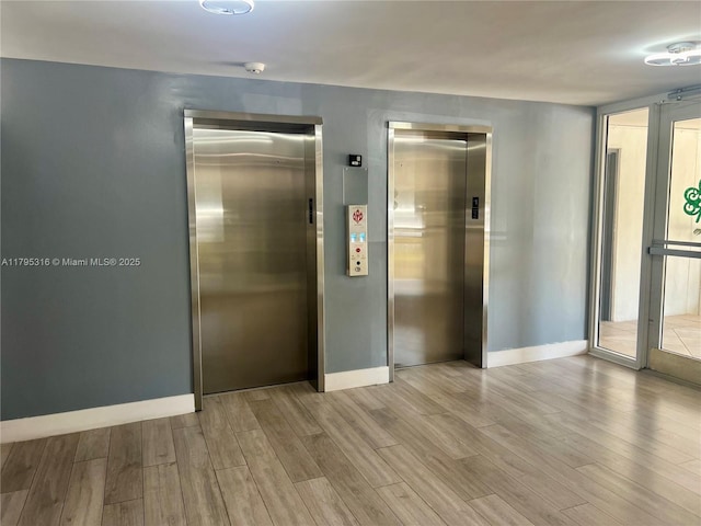 spare room featuring baseboards, elevator, and wood finished floors