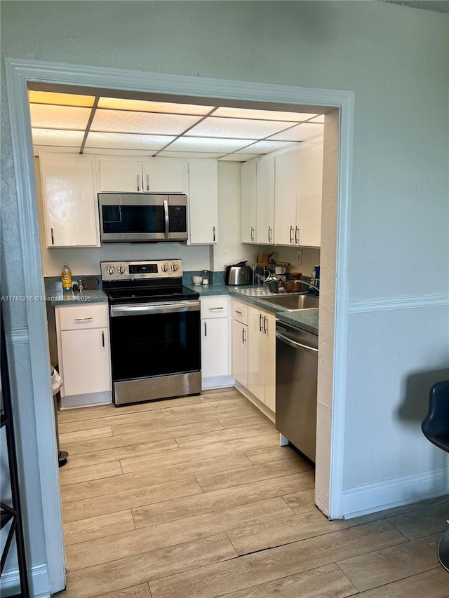 kitchen with a sink, appliances with stainless steel finishes, light wood-type flooring, and dark countertops