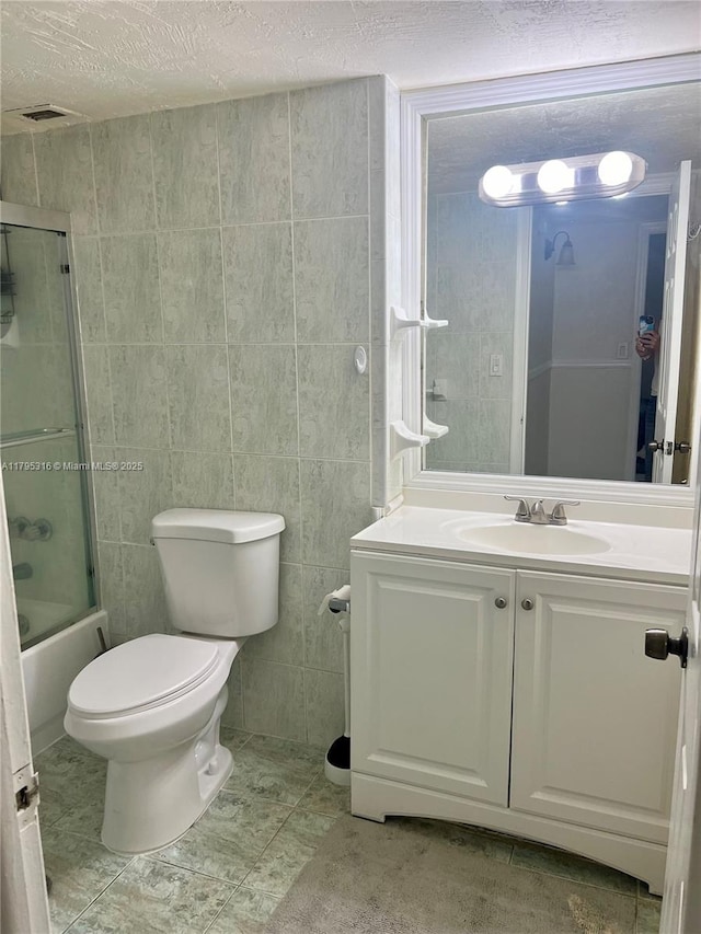 full bathroom featuring vanity, shower / bath combination with glass door, toilet, tile walls, and a textured ceiling