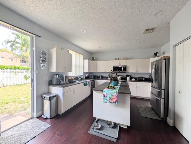 kitchen with visible vents, a kitchen island, dark countertops, a textured ceiling, and appliances with stainless steel finishes