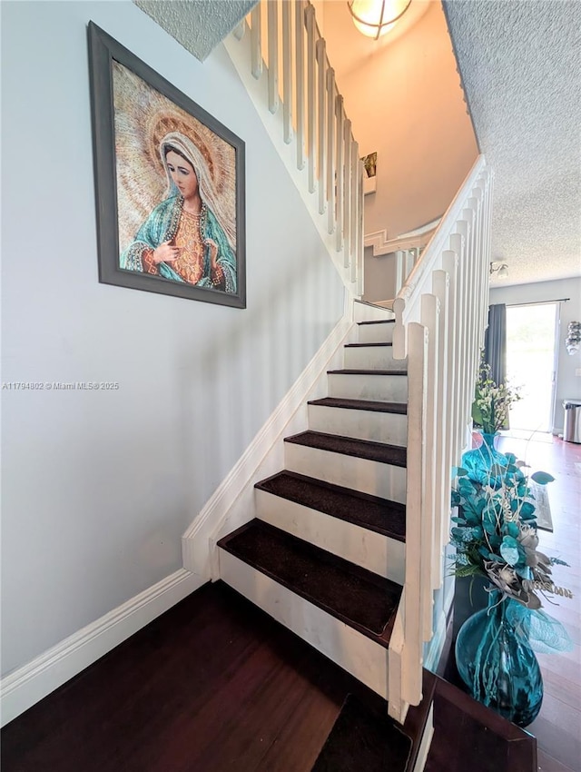 stairway with baseboards, a textured ceiling, and wood finished floors
