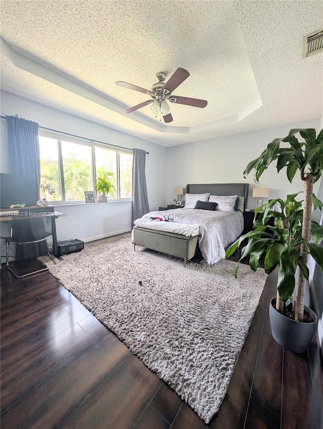 bedroom with visible vents, wood finished floors, ceiling fan, a textured ceiling, and a tray ceiling