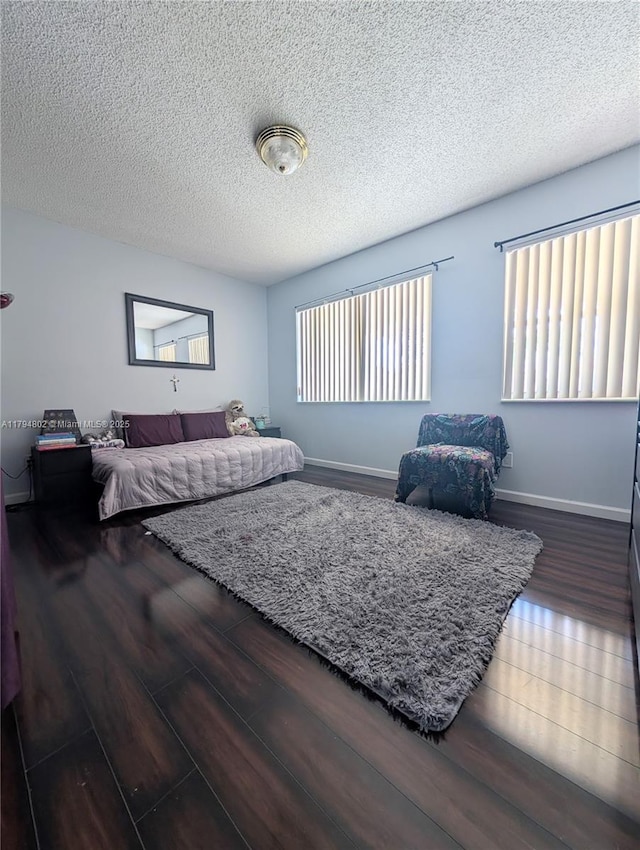 bedroom with a textured ceiling, baseboards, and wood finished floors