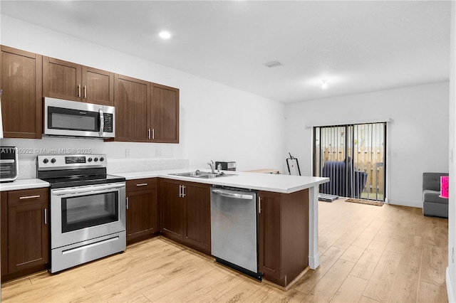 kitchen featuring a sink, stainless steel appliances, a peninsula, and light wood-style flooring