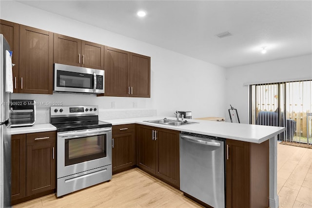 kitchen featuring visible vents, a sink, light wood finished floors, a peninsula, and stainless steel appliances