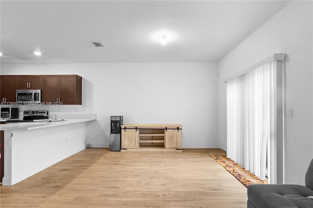kitchen featuring light countertops, appliances with stainless steel finishes, light wood-type flooring, and dark brown cabinets