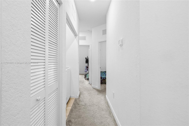 corridor with visible vents, a textured wall, baseboards, and light carpet