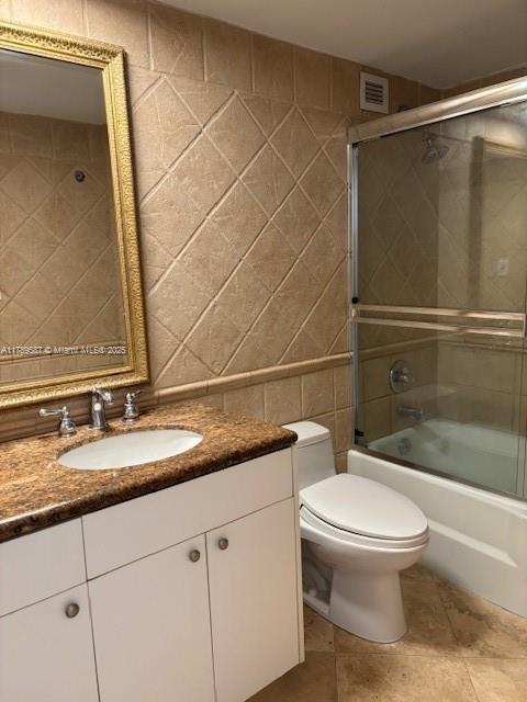bathroom with vanity, tile patterned flooring, toilet, shower / bath combination with glass door, and tile walls