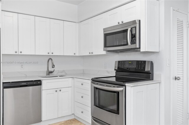 5700 Collins Ave Unit 10D, Miami Beach, FL 33140 - kitchen featuring appliances with stainless steel finishes, white cabinets, and light stone countertops