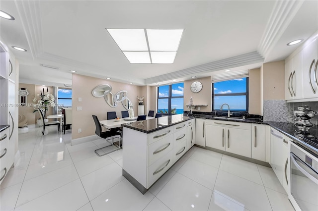 kitchen with plenty of natural light, a sink, a peninsula, a tray ceiling, and oven