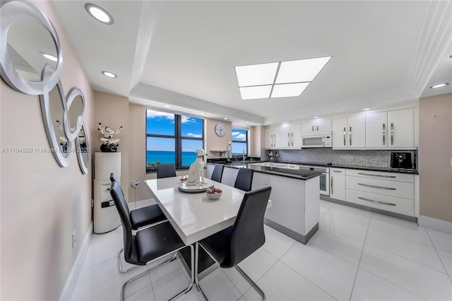 dining area with baseboards, recessed lighting, a raised ceiling, a water view, and a skylight