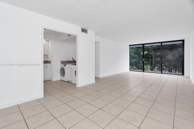 spare room with visible vents, light tile patterned flooring, a wall of windows, baseboards, and a textured ceiling