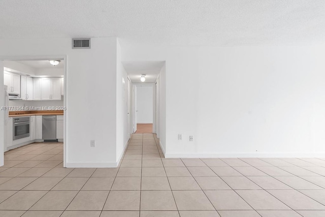 unfurnished room with a textured ceiling, baseboards, light tile patterned flooring, and visible vents