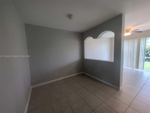 unfurnished room with a ceiling fan, tile patterned floors, baseboards, and arched walkways