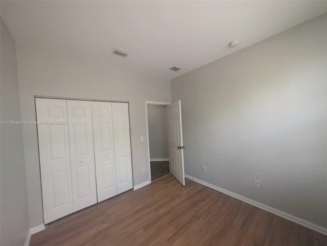 unfurnished bedroom with baseboards, visible vents, wood finished floors, and a closet
