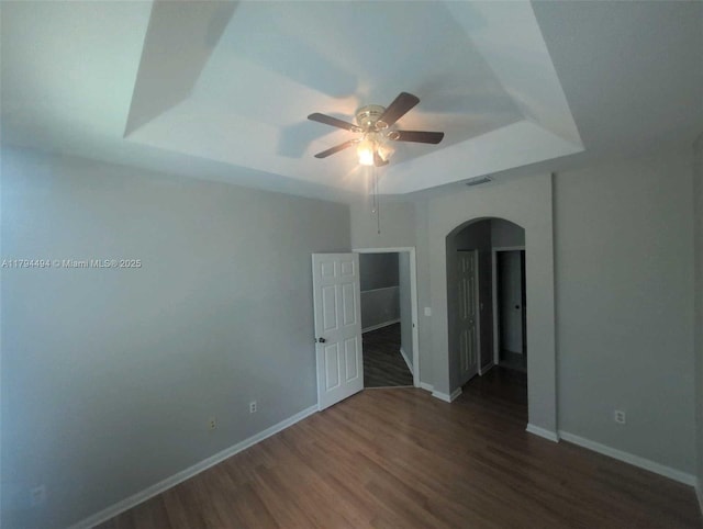 spare room with wood finished floors, baseboards, ceiling fan, a tray ceiling, and arched walkways