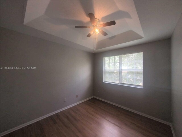empty room with baseboards, a ceiling fan, a tray ceiling, and dark wood finished floors