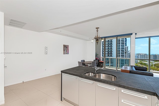 kitchen with visible vents, a view of city, an inviting chandelier, white cabinets, and a sink