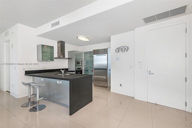 18201 Collins Ave Unit 3405, Sunny Isles Beach, FL 33160 - kitchen featuring visible vents, a peninsula, built in appliances, dark countertops, and wall chimney range hood