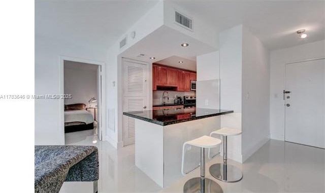 kitchen featuring visible vents, a peninsula, stainless steel microwave, and a breakfast bar area