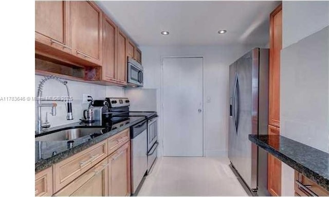 kitchen featuring brown cabinetry, a sink, dark stone countertops, stainless steel appliances, and recessed lighting