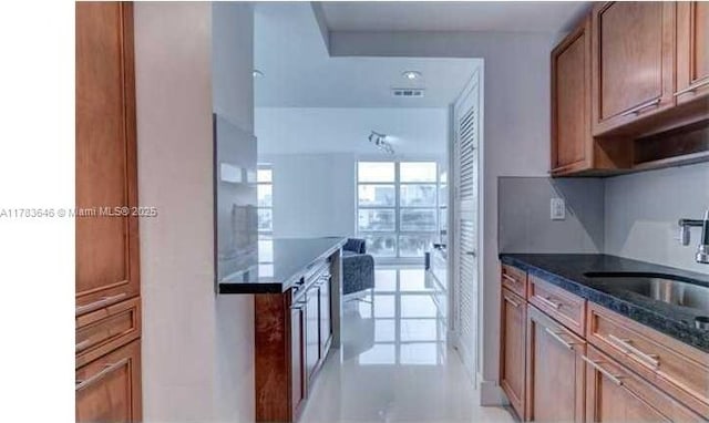 kitchen with visible vents, brown cabinets, a sink, dark stone countertops, and light tile patterned floors