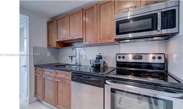 kitchen with a sink, appliances with stainless steel finishes, brown cabinetry, and dark stone counters