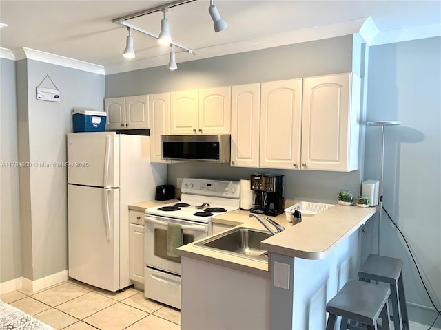 kitchen featuring a kitchen bar, a sink, light tile patterned floors, a peninsula, and white appliances
