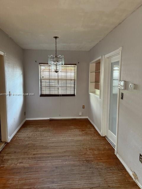 unfurnished dining area with baseboards, wood finished floors, and a notable chandelier