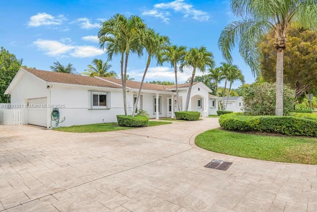 view of front of home with decorative driveway, a garage, a front lawn, and stucco siding