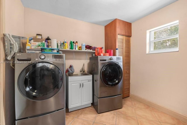 clothes washing area with independent washer and dryer, light tile patterned flooring, baseboards, and cabinet space