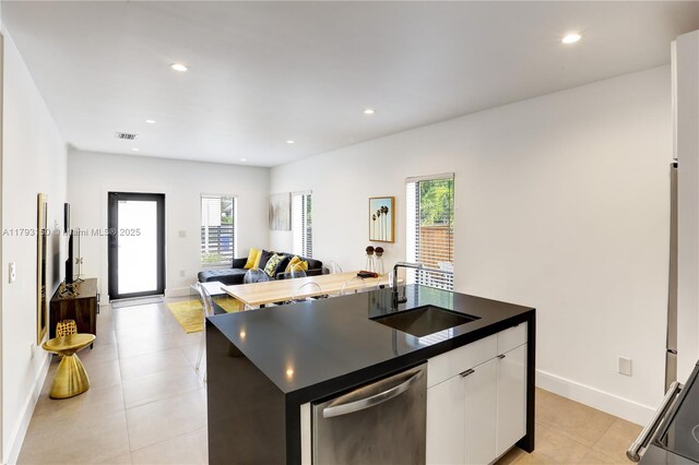 kitchen with dishwasher, a sink, white cabinetry, dark countertops, and an island with sink