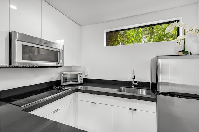 kitchen with dark countertops, stainless steel appliances, white cabinets, and a sink