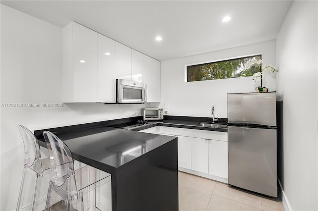 kitchen with a peninsula, a sink, dark countertops, stainless steel appliances, and white cabinets