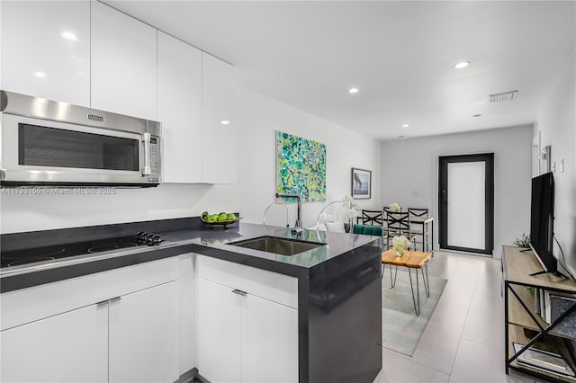 kitchen with a sink, dark countertops, visible vents, stainless steel microwave, and black electric stovetop