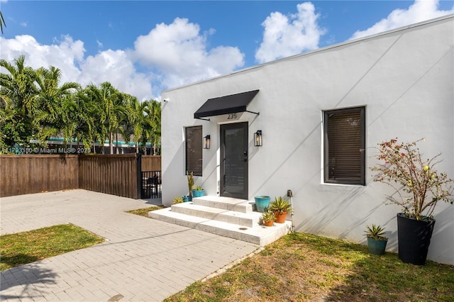entrance to property featuring fence and stucco siding