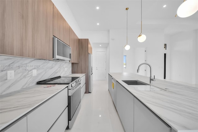 kitchen with modern cabinets, tasteful backsplash, a sink, light stone counters, and stainless steel appliances