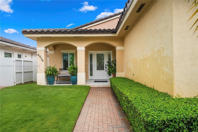 property entrance with a yard, stucco siding, covered porch, and fence
