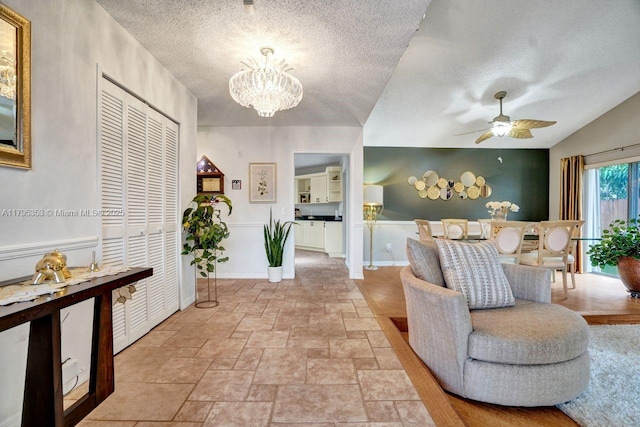 interior space with a textured ceiling, baseboards, ceiling fan with notable chandelier, and stone tile flooring