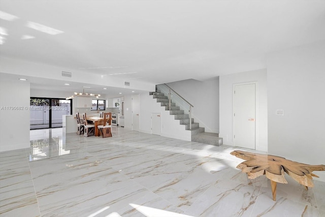 living area with visible vents, a notable chandelier, marble finish floor, stairs, and washer and clothes dryer