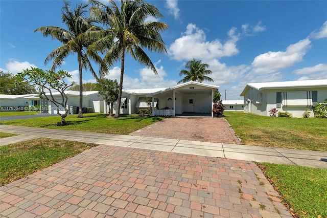 view of front of property with decorative driveway, a carport, a front yard, and stucco siding