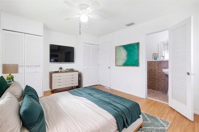 bedroom with a ceiling fan, visible vents, wood finished floors, baseboards, and multiple closets