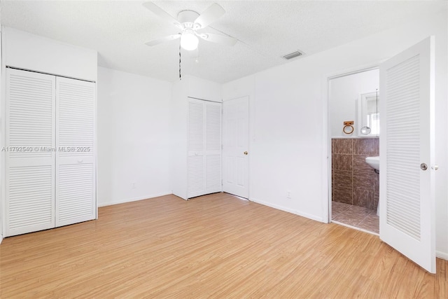 unfurnished bedroom with two closets, baseboards, ensuite bathroom, light wood-type flooring, and visible vents