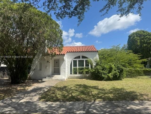 mediterranean / spanish house featuring a front lawn, stucco siding, and a tiled roof