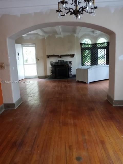unfurnished living room featuring arched walkways, a fireplace, hardwood / wood-style flooring, baseboards, and a chandelier