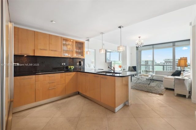 kitchen featuring glass insert cabinets, open floor plan, tasteful backsplash, a sink, and a notable chandelier