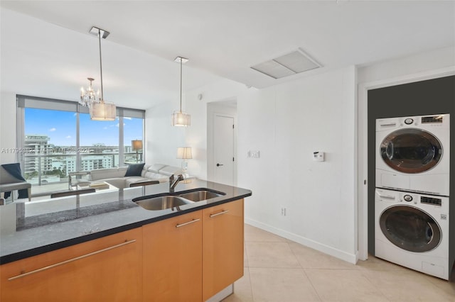 kitchen featuring stacked washer and clothes dryer, baseboards, a sink, dark stone countertops, and decorative light fixtures