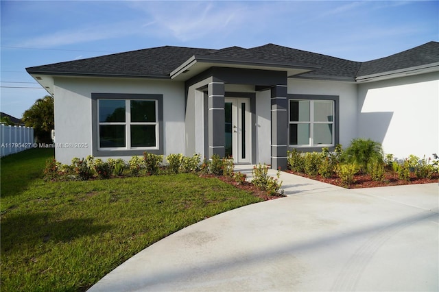 view of front facade with fence, a shingled roof, a front lawn, and stucco siding