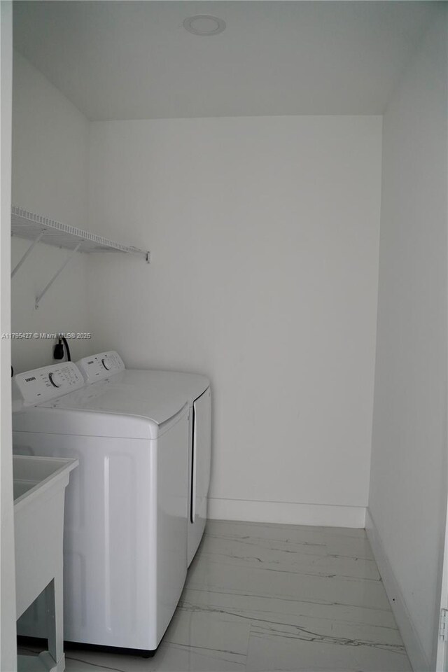 clothes washing area featuring baseboards, laundry area, marble finish floor, and washing machine and clothes dryer