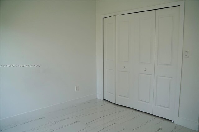 unfurnished bedroom with baseboards, marble finish floor, and a closet